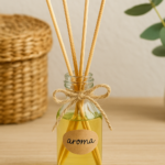 Aromatizador caseiro de varetas com líquido amarelo claro em frasco de vidro decorado com laço de sisal, sobre superfície de madeira clara, ao lado de ramo de eucalipto