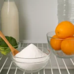 Interior de uma geladeira limpa e organizada com potes de vidro, frutas frescas e pote aberto com bicarbonato de sódio sobre a prateleira
