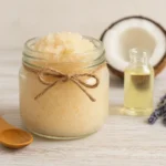 Esfoliante corporal caseiro com açúcar e óleo de coco em pote de vidro decorado com barbante, ao lado de óleo vegetal, coco e lavanda